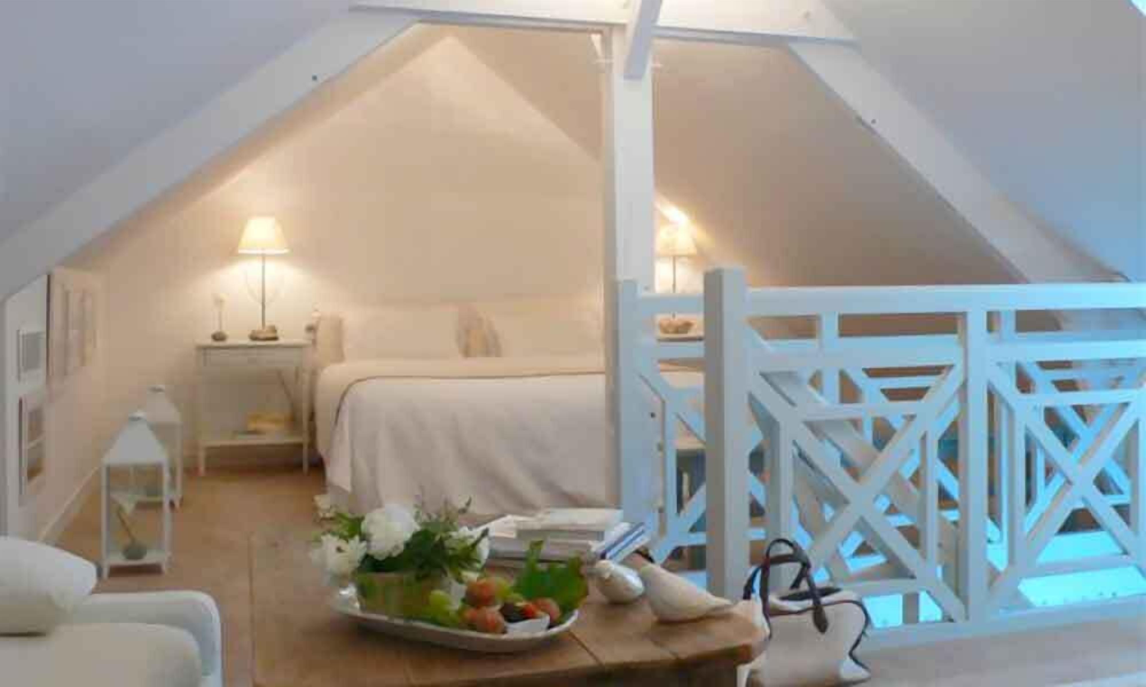 Une chambre confortable située dans les combles, avec un lit, une table de chevet, une lampe et une vue sur l’extérieur.