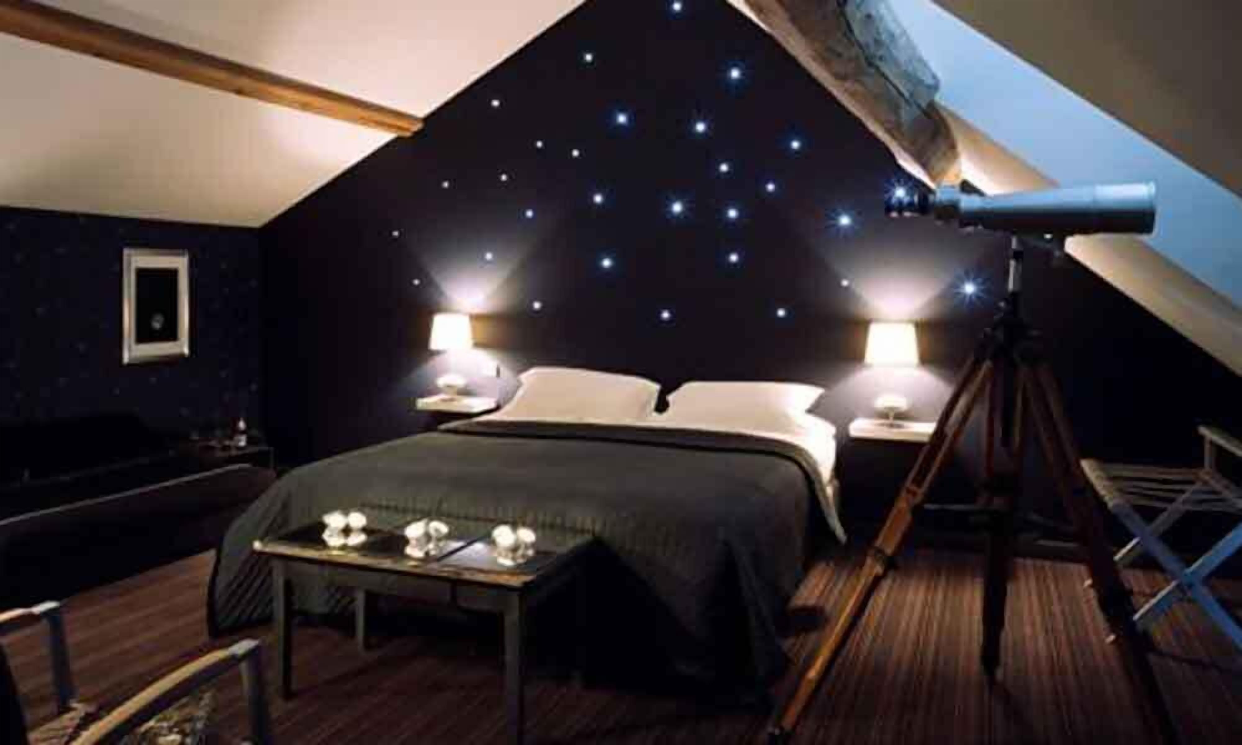 Un dormitorio con techo estrellado, un telescopio y una cama con mesita de noche.