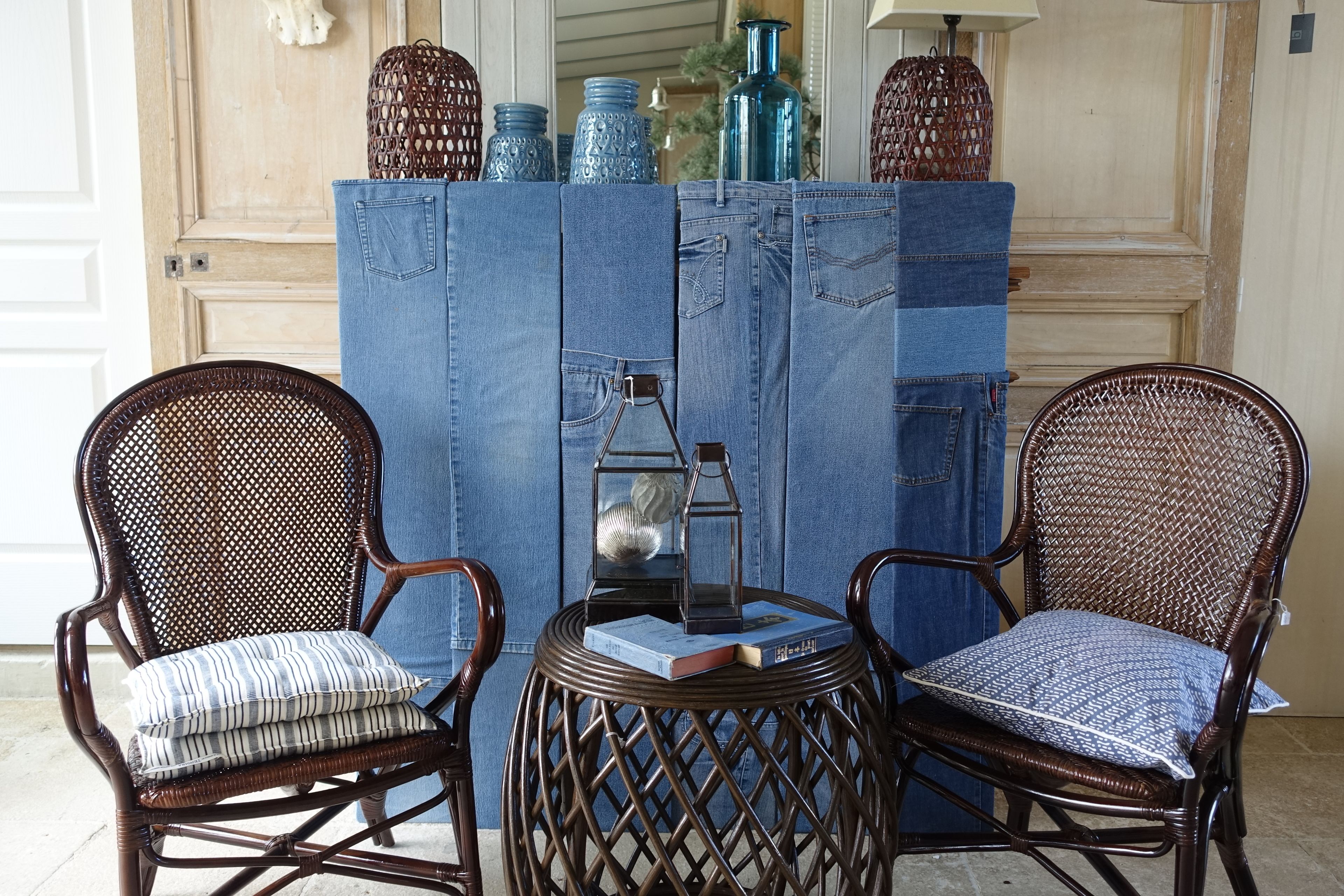 Dos sillones de mimbre con cojines, una mesita redonda con un farol, y un fondo de tela vaquera decorado con objetos decorativos.