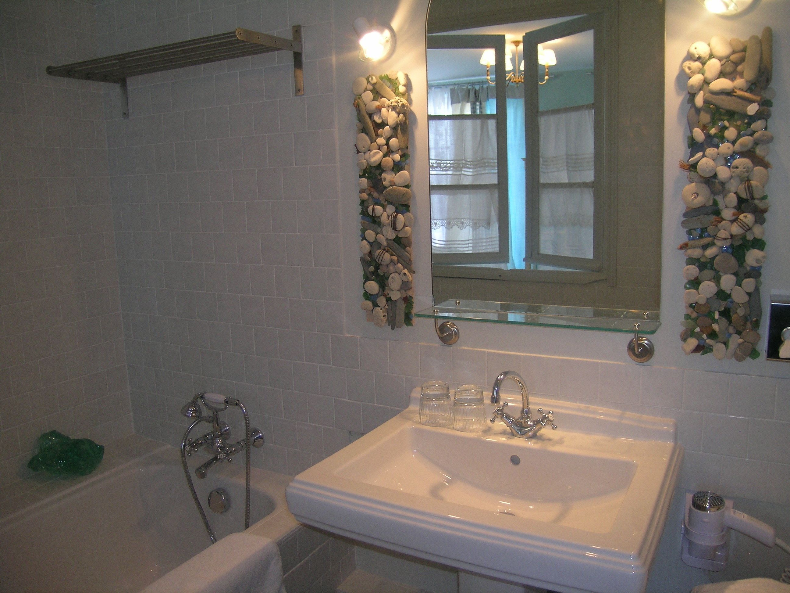 A bathroom with a white sink, a bathtub, and a mirror with decorative stones.