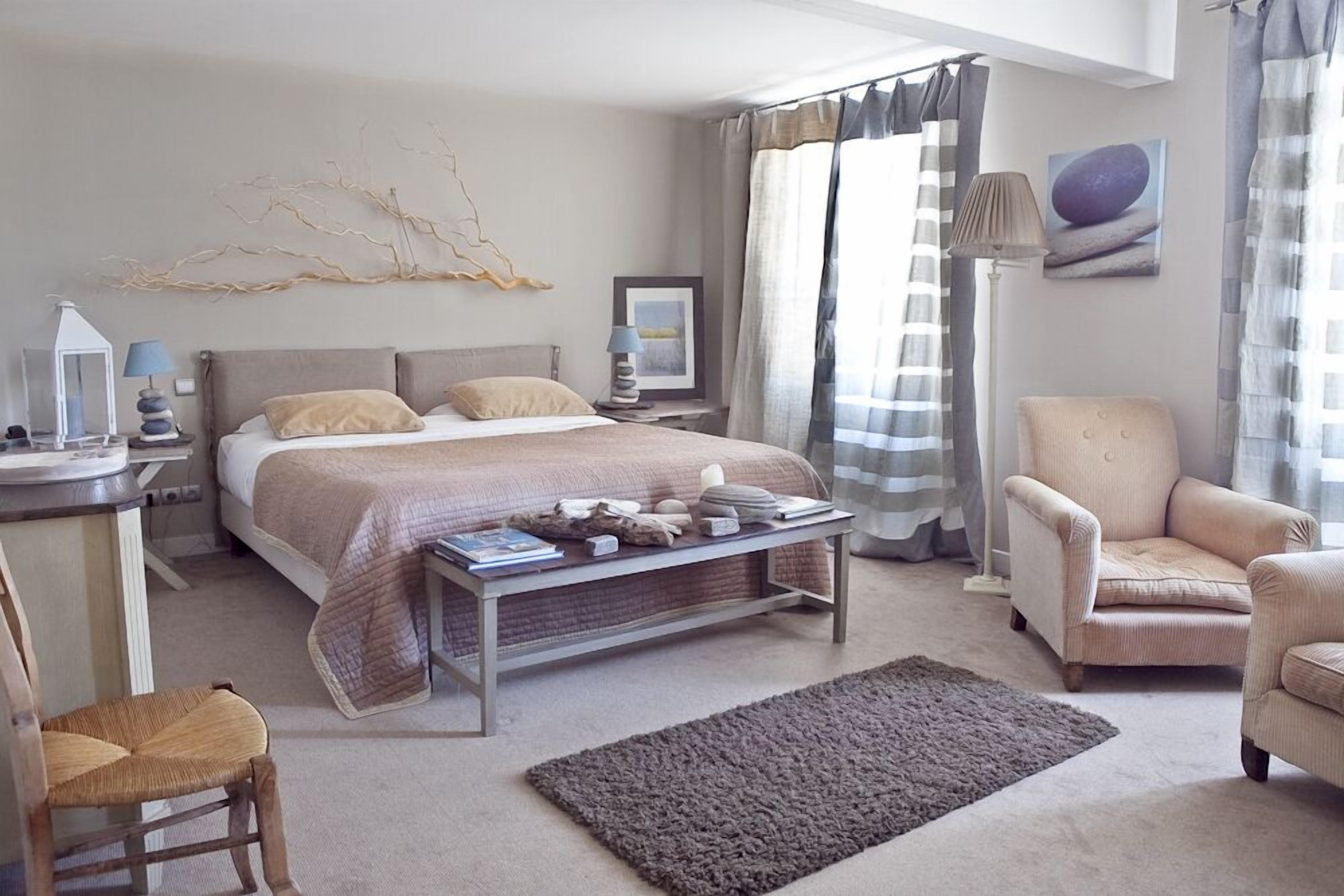 A modern bedroom with a bed, bedside table, lamp, chair, and a view of the outdoors.