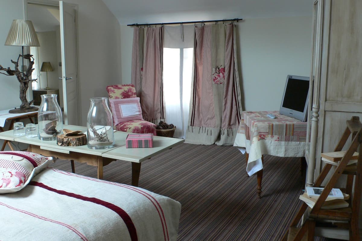 Habitació acollidora amb un llit, un escriptori amb una làmpada, una cadira, una televisió i una finestra amb cortines.