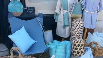 A storefront with a beach-themed mural, a table with a sign, and various home decor items like cushions, a lamp, and a mannequin dressed in a striped shirt.