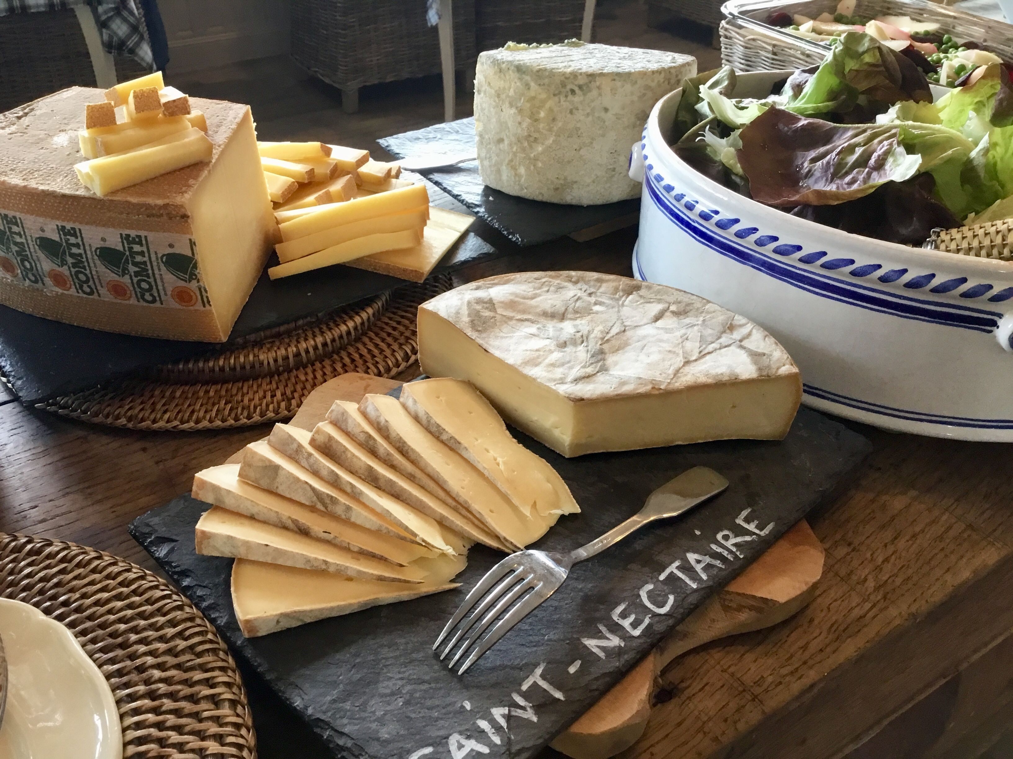 A variety of cheeses and a bowl of salad on a wooden table.