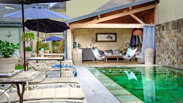 Relax by the pool with lounge chairs and a table, surrounded by a covered patio and stone wall.