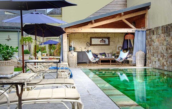 Zona junto a la piscina con sillones de descanso, una mesa y sombrillas.