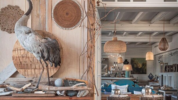 Un intérieur rustique avec une table à manger en bois, des chaises en osier et une grande sculpture d’oiseau.