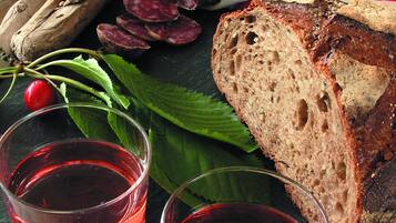 A wooden tray with sliced bread, a whole baguette, fresh herbs, and two glasses of red liquid.