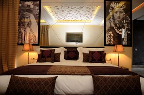 A hotel room with a large bed, patterned pillows, two wall-mounted lamps, and two framed pictures on the walls.