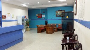 A reception area with a blue counter, wooden chairs, a small table, and a refrigerator. - PD Sea Front Hotel (Port Dickson)