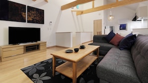 Ein modernes Wohnzimmer mit Flachbildfernseher, Couchtisch aus Holz, grauem Sofa und einem schwarz-weißen Teppich.