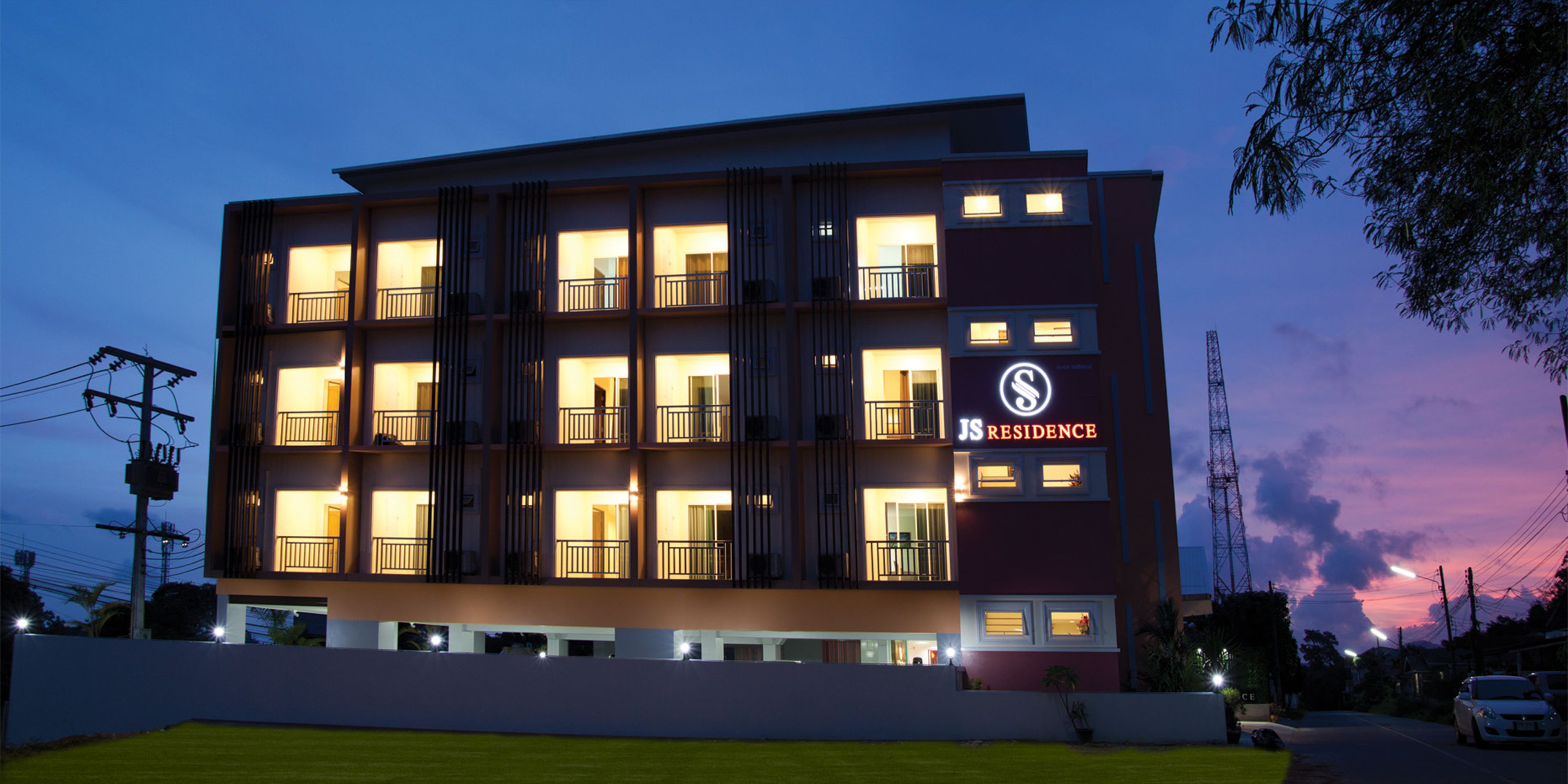 Et hotel med flere etager, oplyste balkoner og et skilt, der siger "JS Residence".