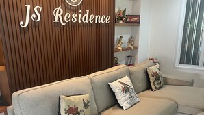 A modern living room with a sectional sofa, decorative pillows, and a wooden accent wall with the logo "JS Residence". - JS Residence Krabi (Krabi)