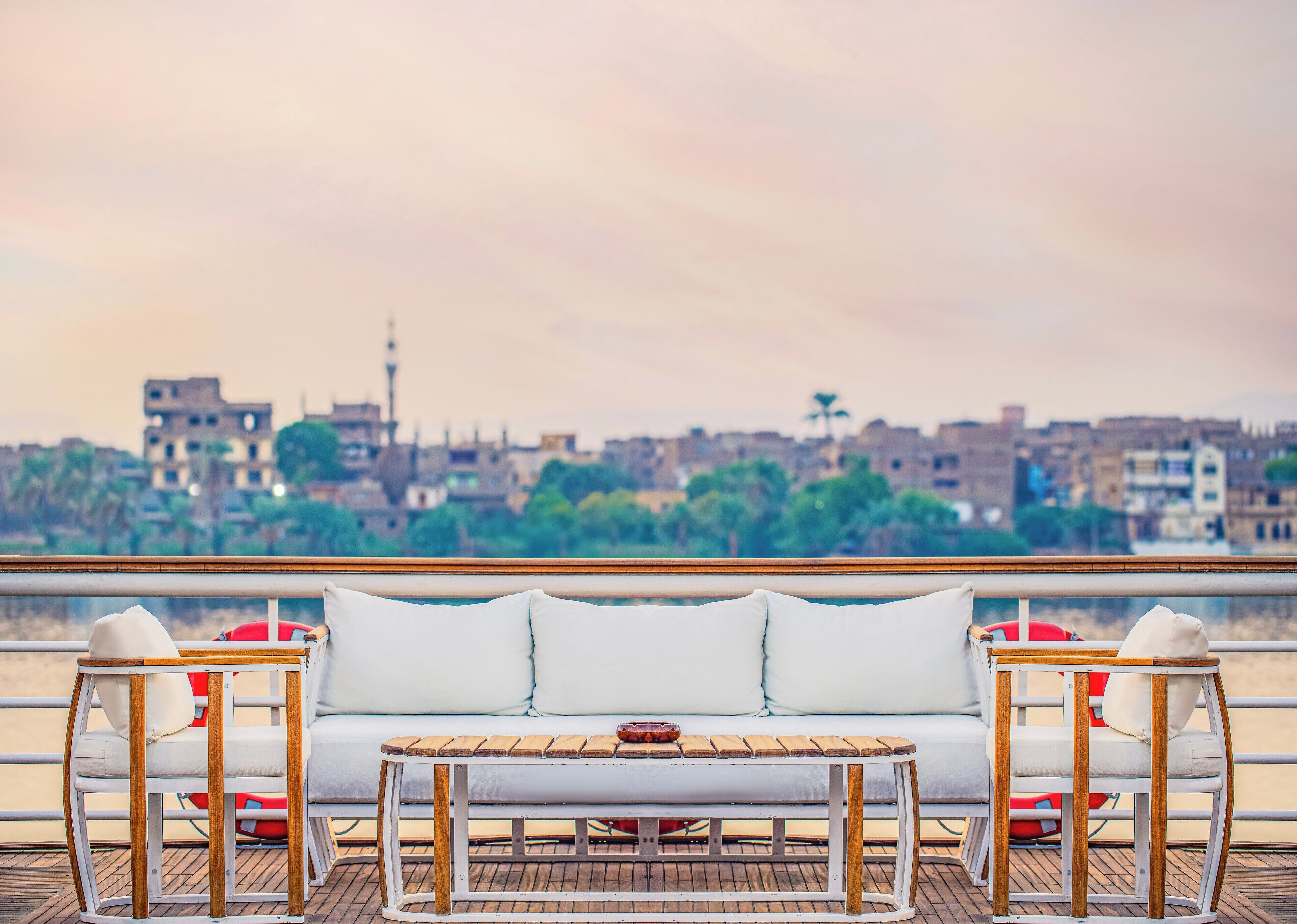 Un canapé blanc et une table en bois sur un balcon avec vue sur la ville.