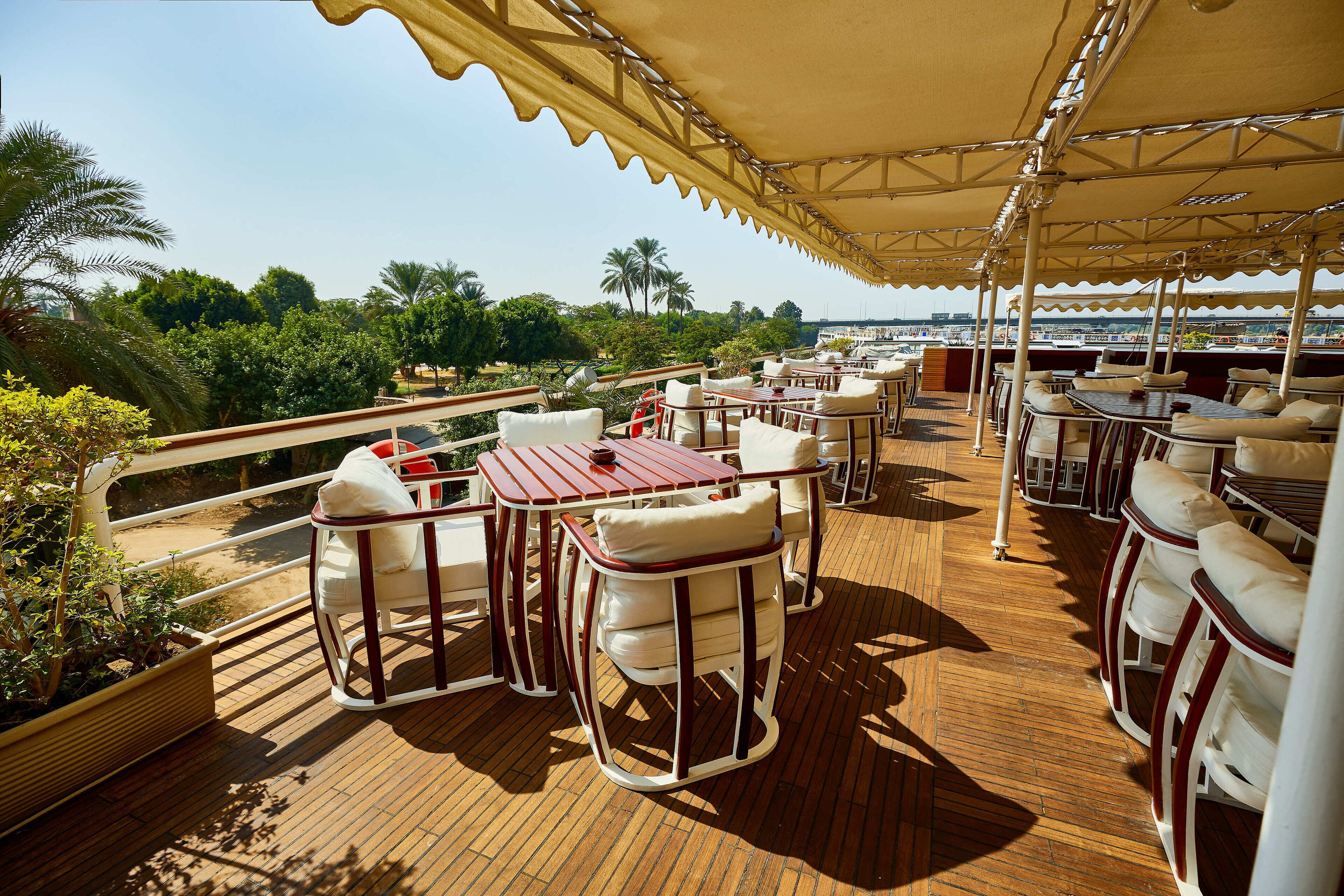 Une terrasse extérieure avec des tables et des chaises, offrant une vue panoramique sur un paysage agrémenté de palmiers et d’une côte lointaine.