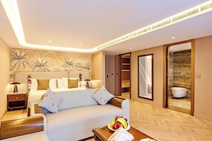A hotel room with a bed, a sofa, a bedside table with a lamp, a fruit bowl, and a bathroom visible through an open door. - Sonesta St George Nile Cruise  Ship - 3 & 7 Nights - From  Aswan  Every Friday (Luxor)