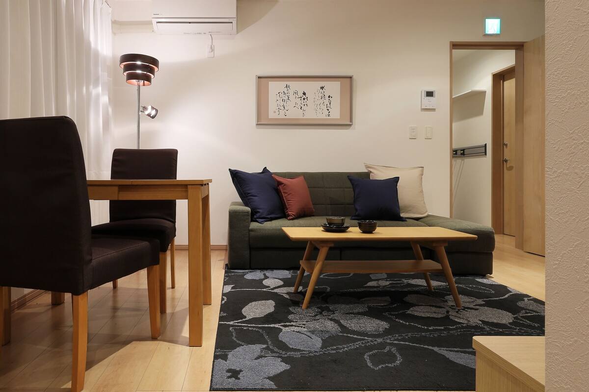 Un salon moderne avec une table à manger en bois, un canapé avec des coussins, une lampe sur pied et une œuvre d’art encadrée accrochée au mur.
