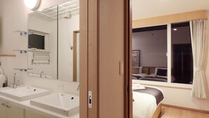 Ein modernes Hotelzimmer mit einem großen Spiegel, zwei Waschbecken, einem Bett und einem Fenster mit Vorhängen.