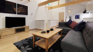 Ein modernes Wohnzimmer mit Flachbildfernseher, Couchtisch aus Holz, grauem Sofa und einem schwarz-weißen Teppich.