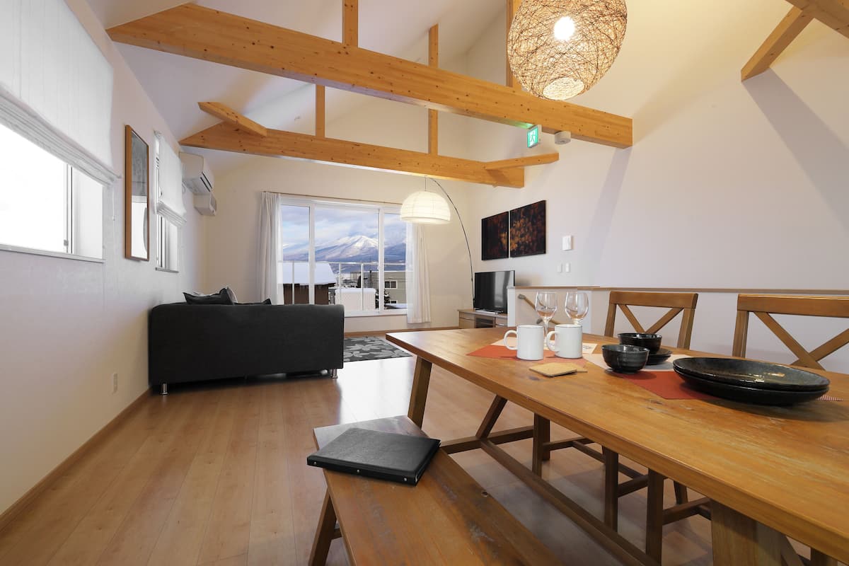 Une cuisine moderne avec des poutres en bois, une table à manger avec des bols, un banc et une vue sur une montagne par la fenêtre.