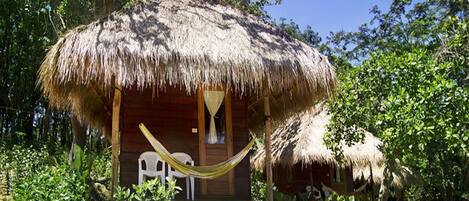 A thatched-roof hut with a hammock, surrounded by lush greenery.