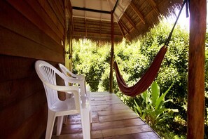 A wooden porch with a thatched roof, white plastic chairs, and a hammock.