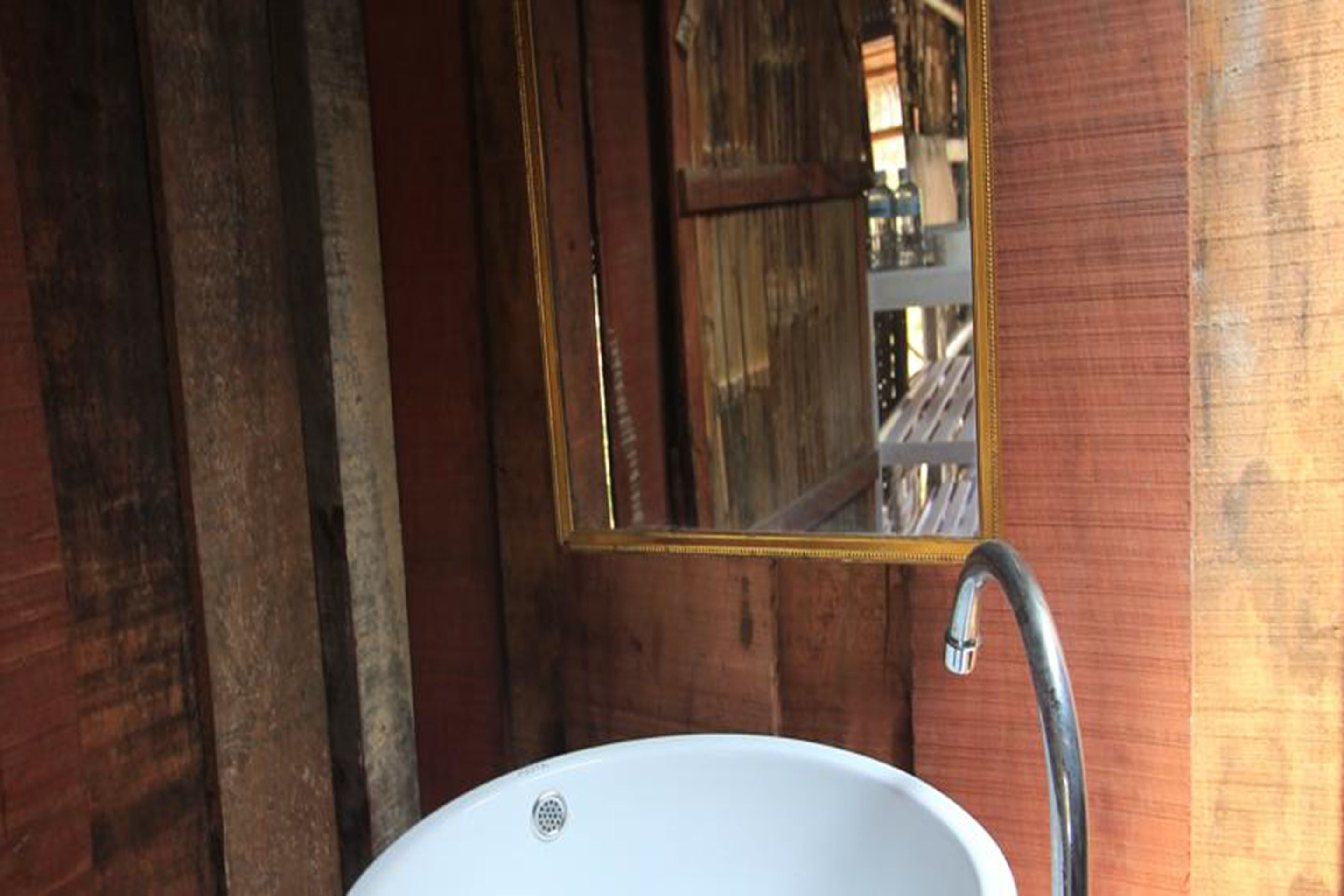 Une salle de bain rustique en bois, avec un lavabo blanc et un miroir.