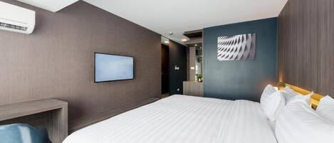 A modern hotel room with a large bed, a desk, and a flat-screen TV on the wall.