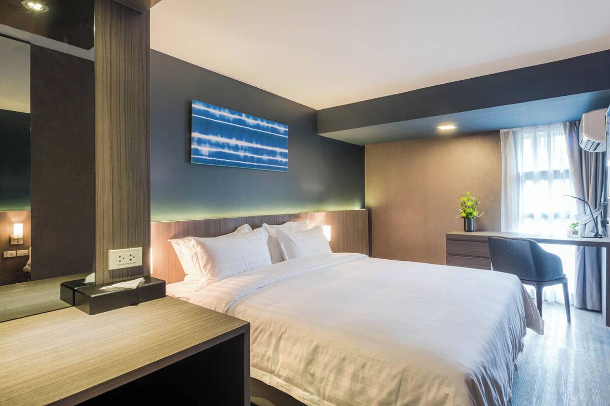 A modern hotel room with a large bed, a desk, and a small plant.