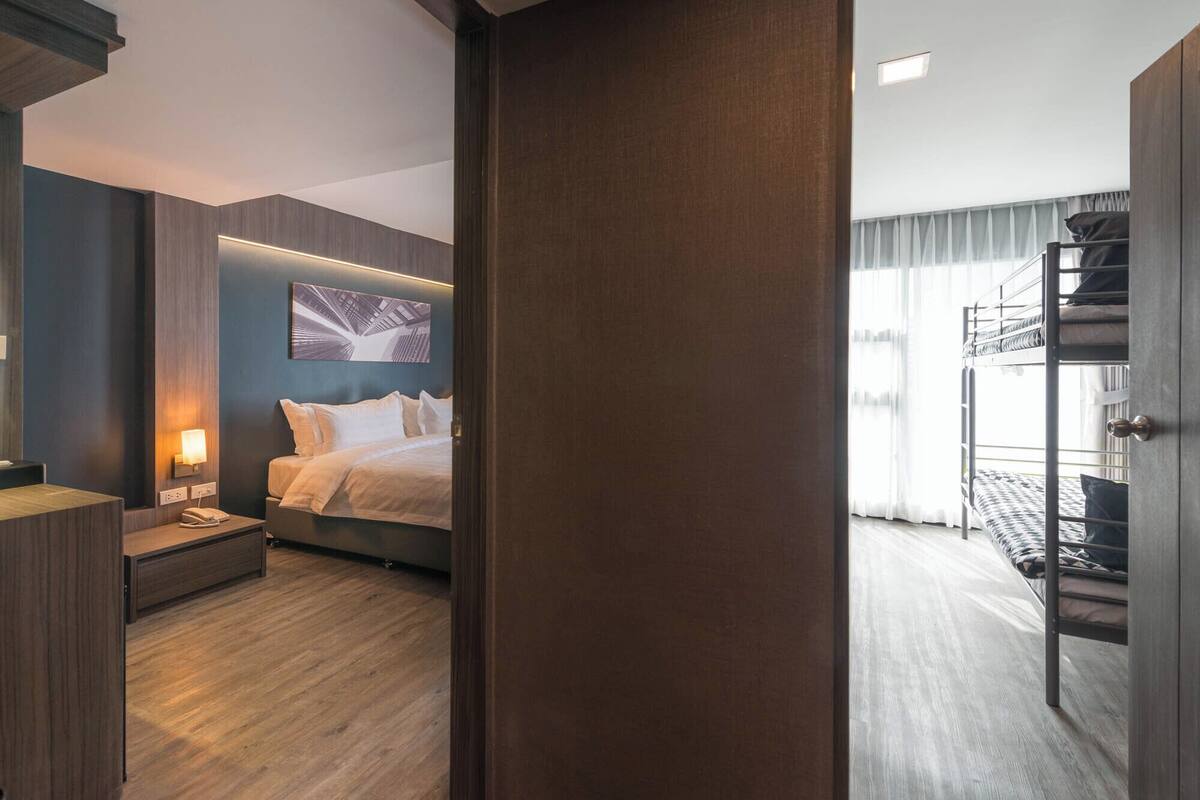 A hotel room with a bed, bedside table, lamp, and a view of the city through the window.