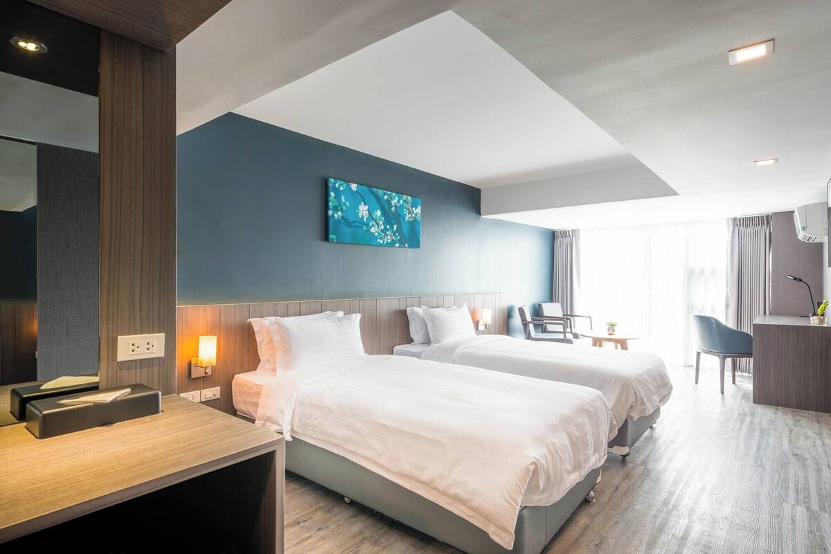 A hotel room with two beds, a desk, a chair, and a small table.