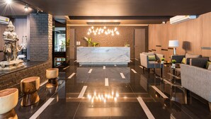 A modern lobby with a marble reception desk, a statue, and a seating area with sofas and a coffee table. - Fyn Hotel (Bangkok)