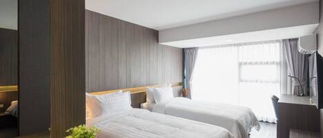 A hotel room with two beds, a desk, a mirror, and a window with curtains.