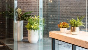 A modern hotel lobby with glass walls, a brick wall, and potted plants. - Fyn Hotel (Bangkok)