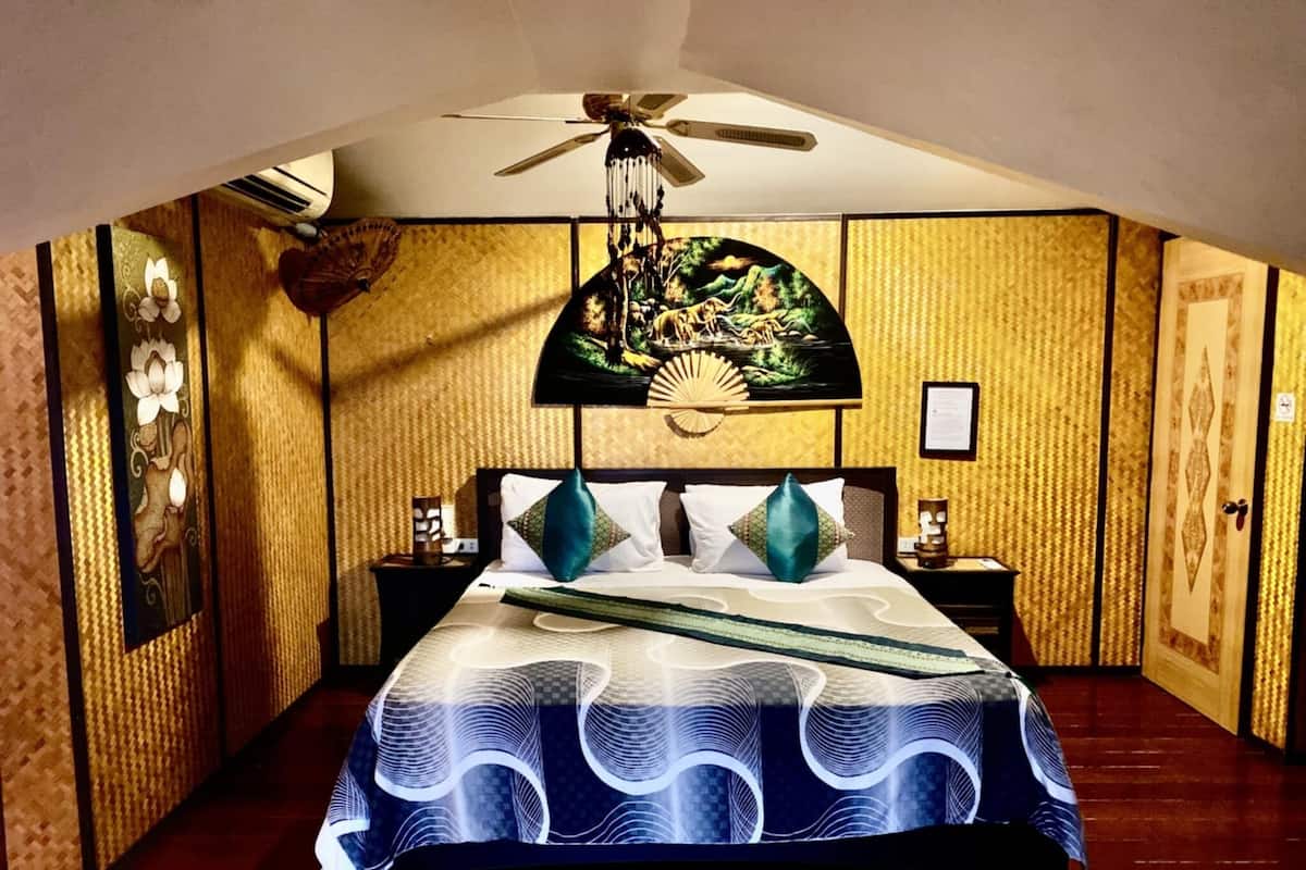 A bedroom with a bed, a ceiling fan, a nightstand, a wall-mounted fan, and a decorative wall panel.