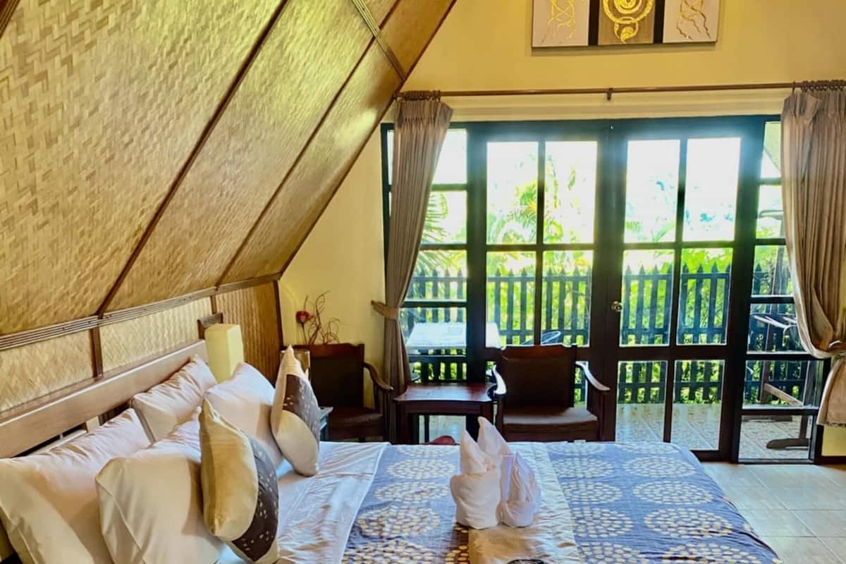 A spacious bedroom with a large bed, a wooden headboard, and a view of the outdoors through a large window.
