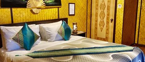 Uma cama com colcha estampada, um ventilador de teto e um ventilador decorativo fixado na parede.