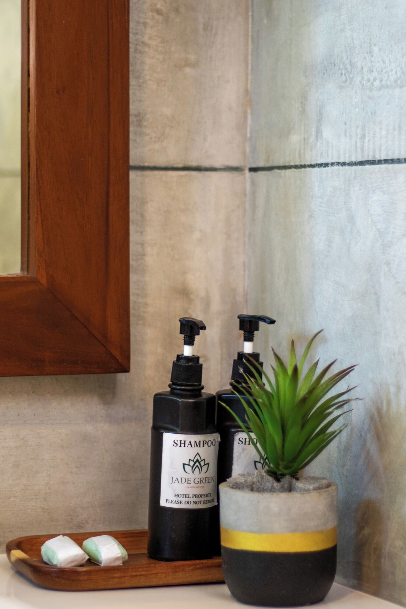 Two bottles of Jade Green hotel shampoo, a potted plant, and a tray with two soap bars.