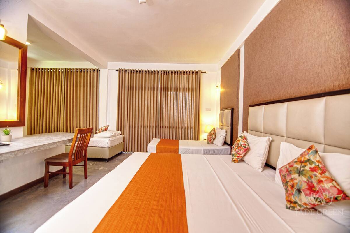 Une chambre d’hôtel avec un grand lit, un bureau et une chaise. Il y a des rideaux et une tête de lit.