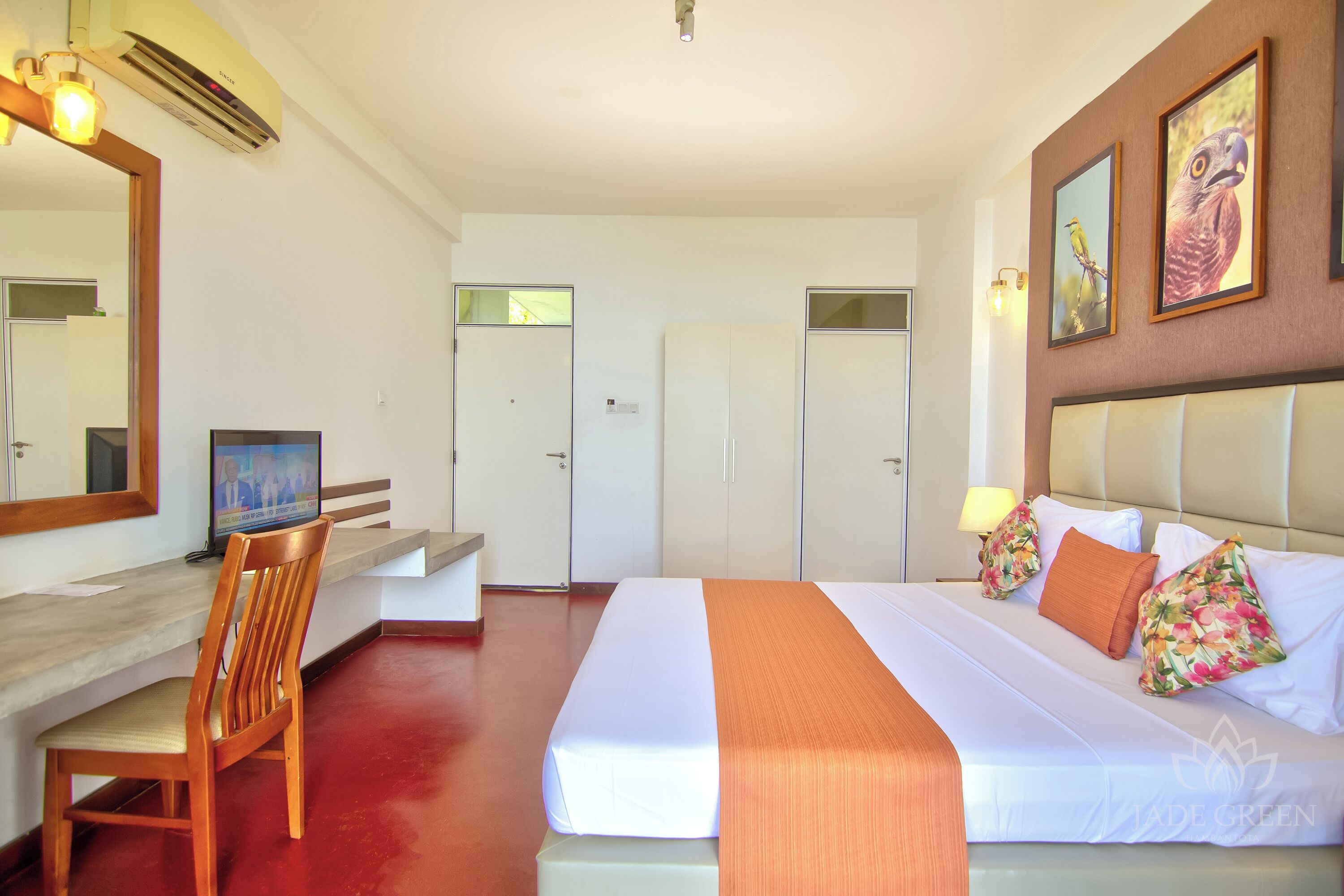 Een hotelkamer met een bed, een bureau met stoel, een garderobe en een spiegel.