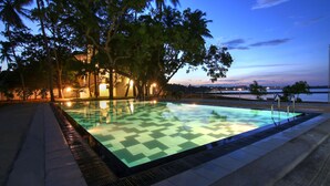 Una piscina exterior con diseño a cuadros, rodeada de árboles y un edificio con luces.