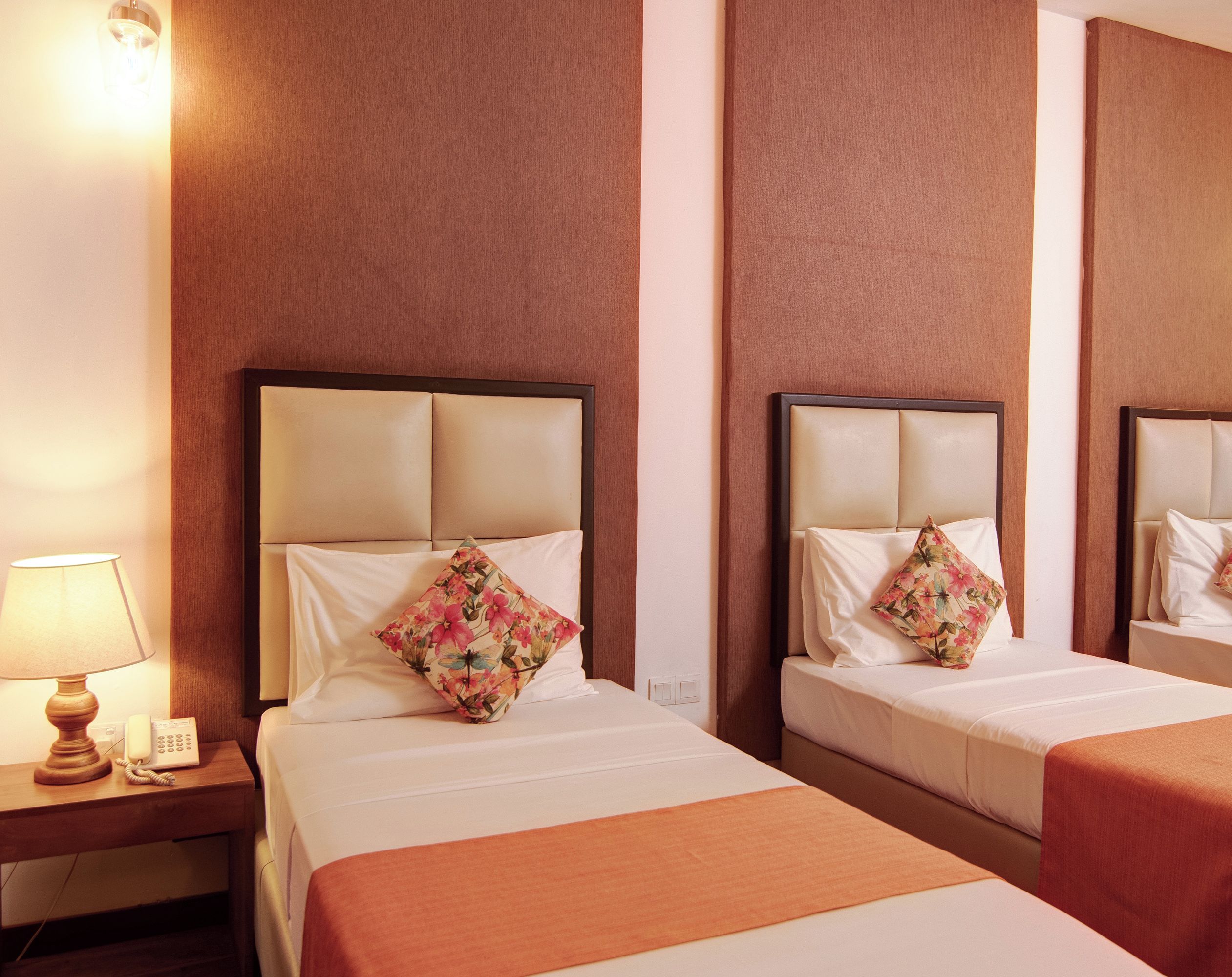 A hotel room with three beds, each with a headboard, a nightstand with a lamp, and a telephone.