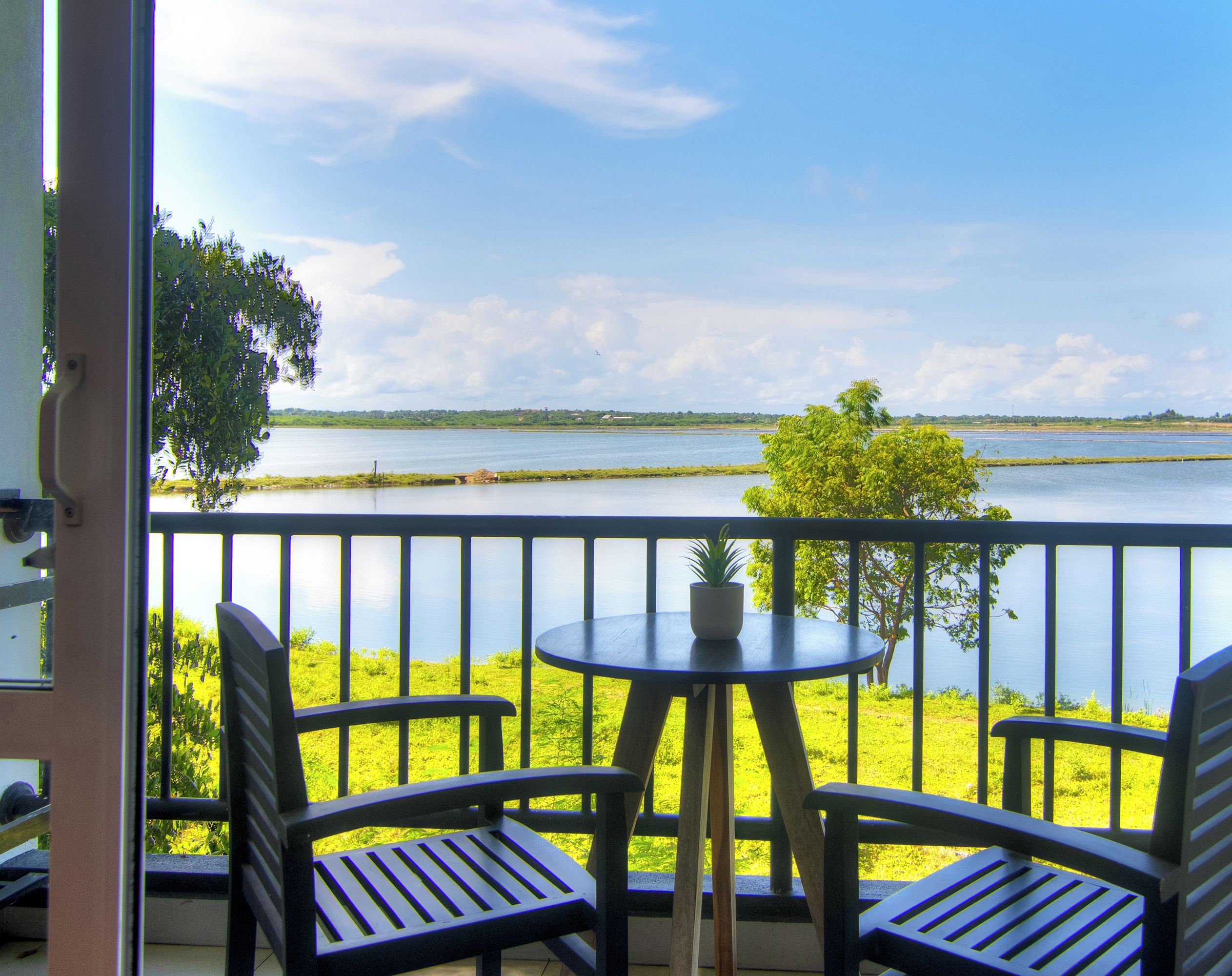 Un balcon avec deux chaises et une petite table, donnant sur une étendue d’eau calme et une végétation luxuriante.