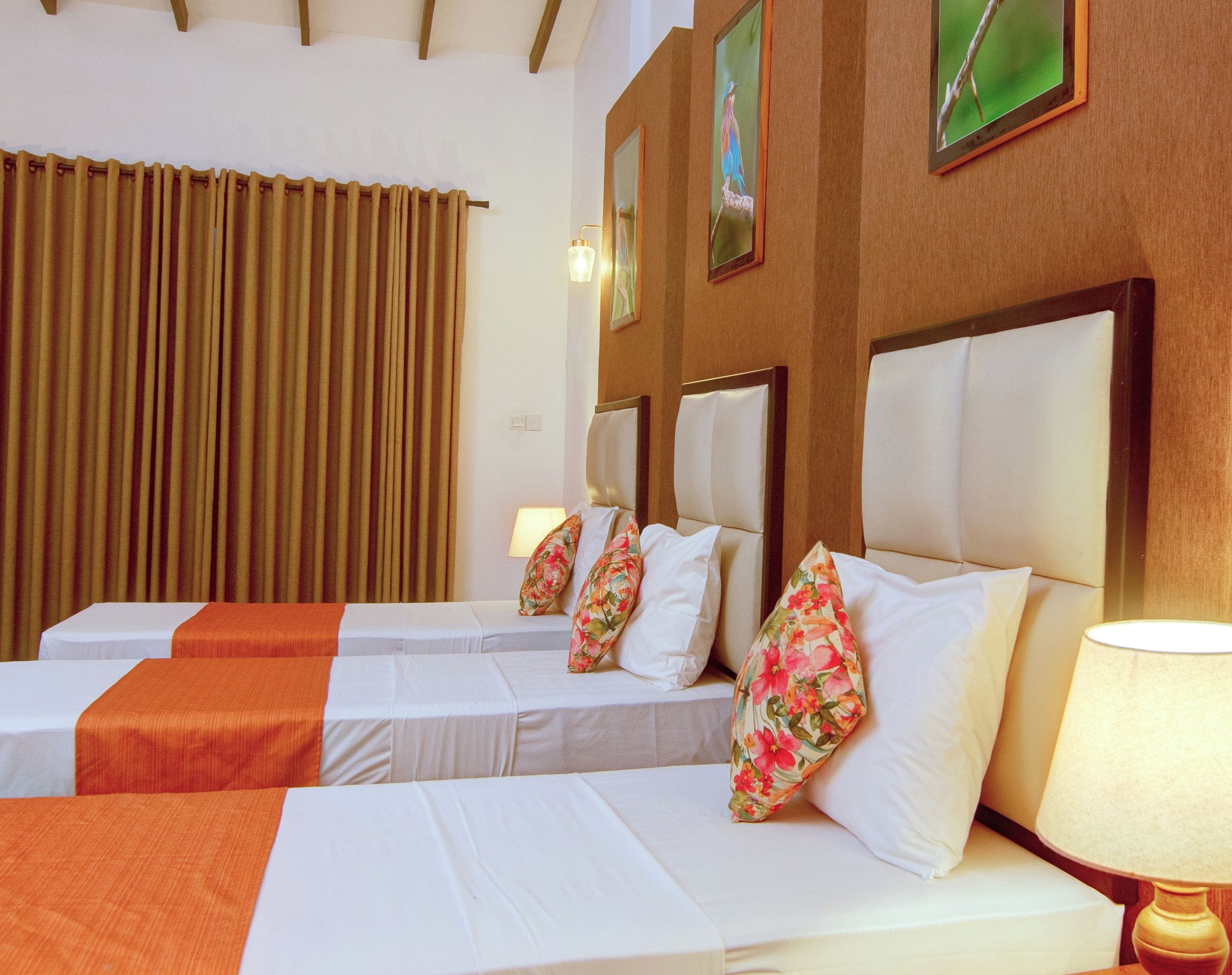 A hotel room with two beds, each with a white bedspread and orange accents, a wooden headboard, and a nightstand with a lamp.