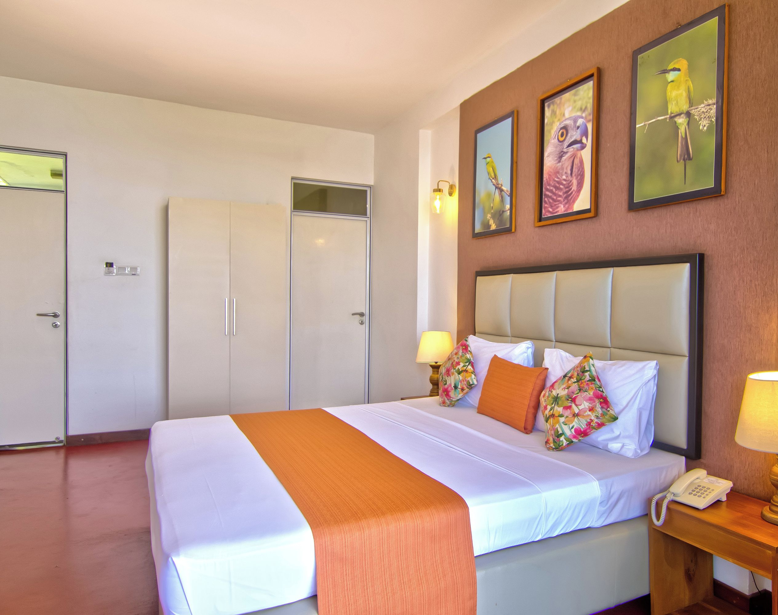 A hotel room with a bed, bedside lamps, a telephone, and framed artwork on the wall.
