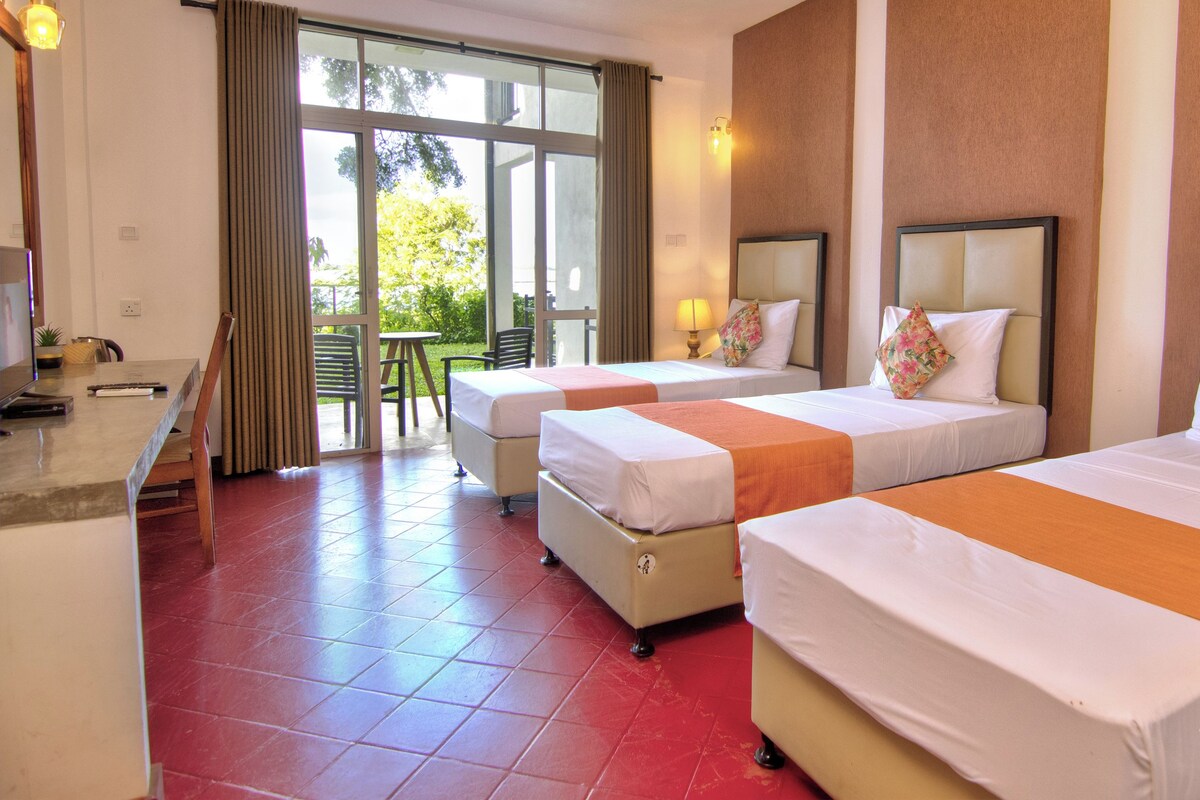 Habitación de hotel con tres camas, un escritorio y vistas al exterior.