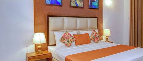 A neatly made bed with a white and orange bedspread, flanked by two nightstands with lamps, and three framed peacock images on the wall above.