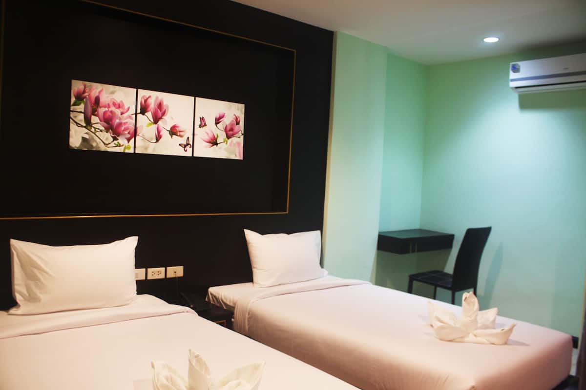 A hotel room with two beds, a desk, and a wall-mounted air conditioner.