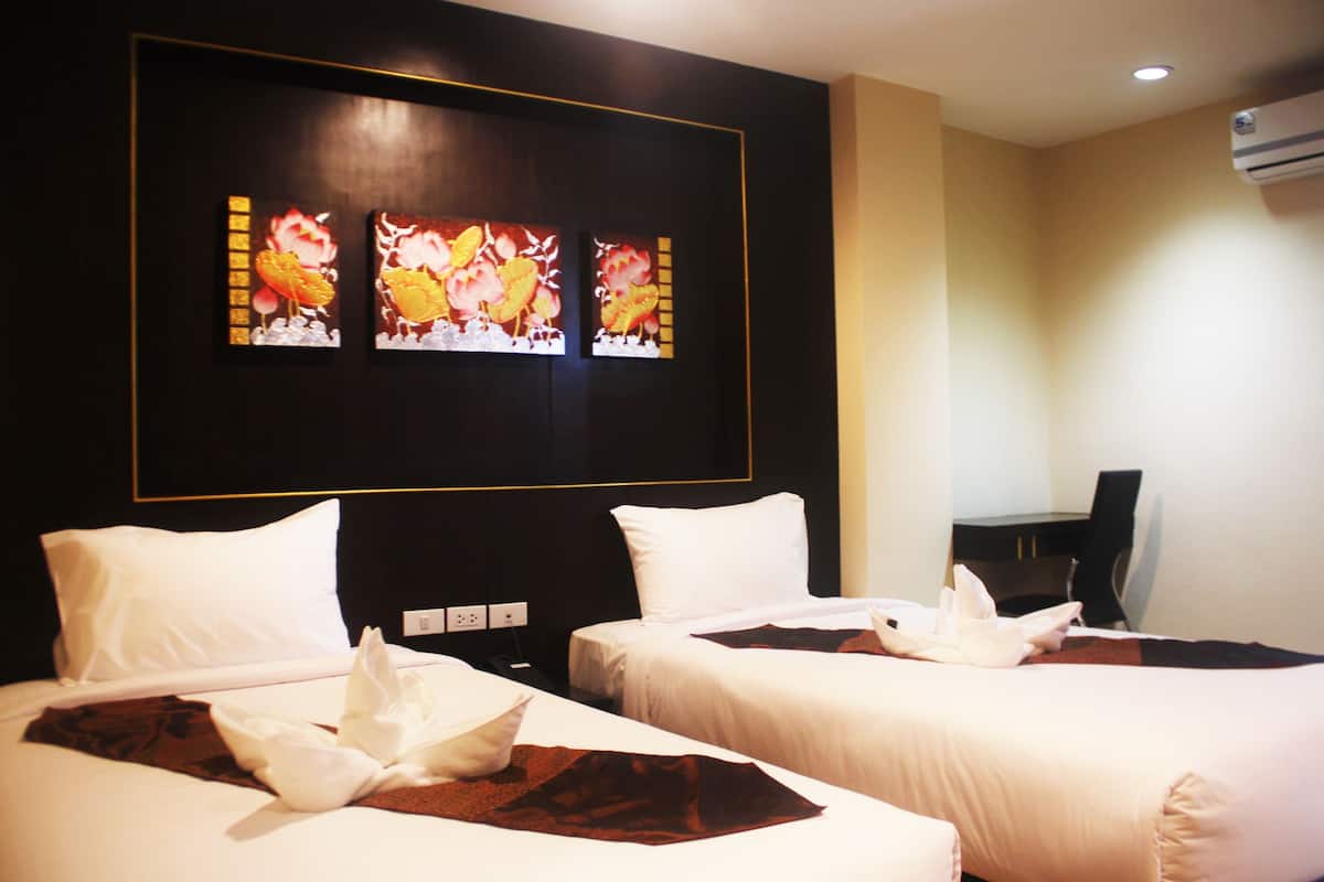 A hotel room with two beds, white bedding, a dark wall with a floral artwork, and a desk with a chair.