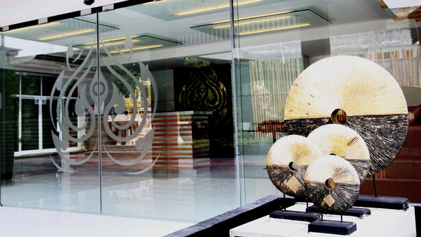 A modern building with glass windows reflecting interior lights and decorative elements. - Metro Hotel & Spa (Thung Song)